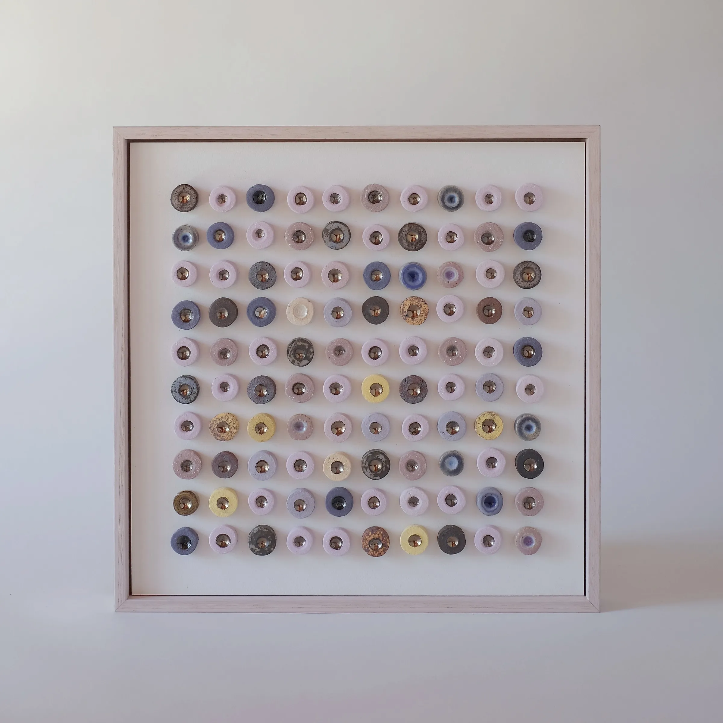 Dot Drift Duo (Suvarna) by Minaal Lawn, a framed grid of one hundred pink, lilac and slate glazed ceramic discs with lustre centres