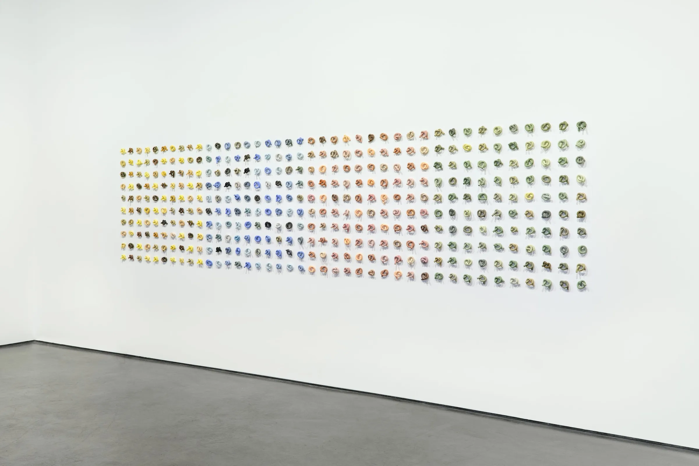 Not Wall No. 3, a grid of 400 small ceramic knots on a gallery wall, with a visitor walking past
