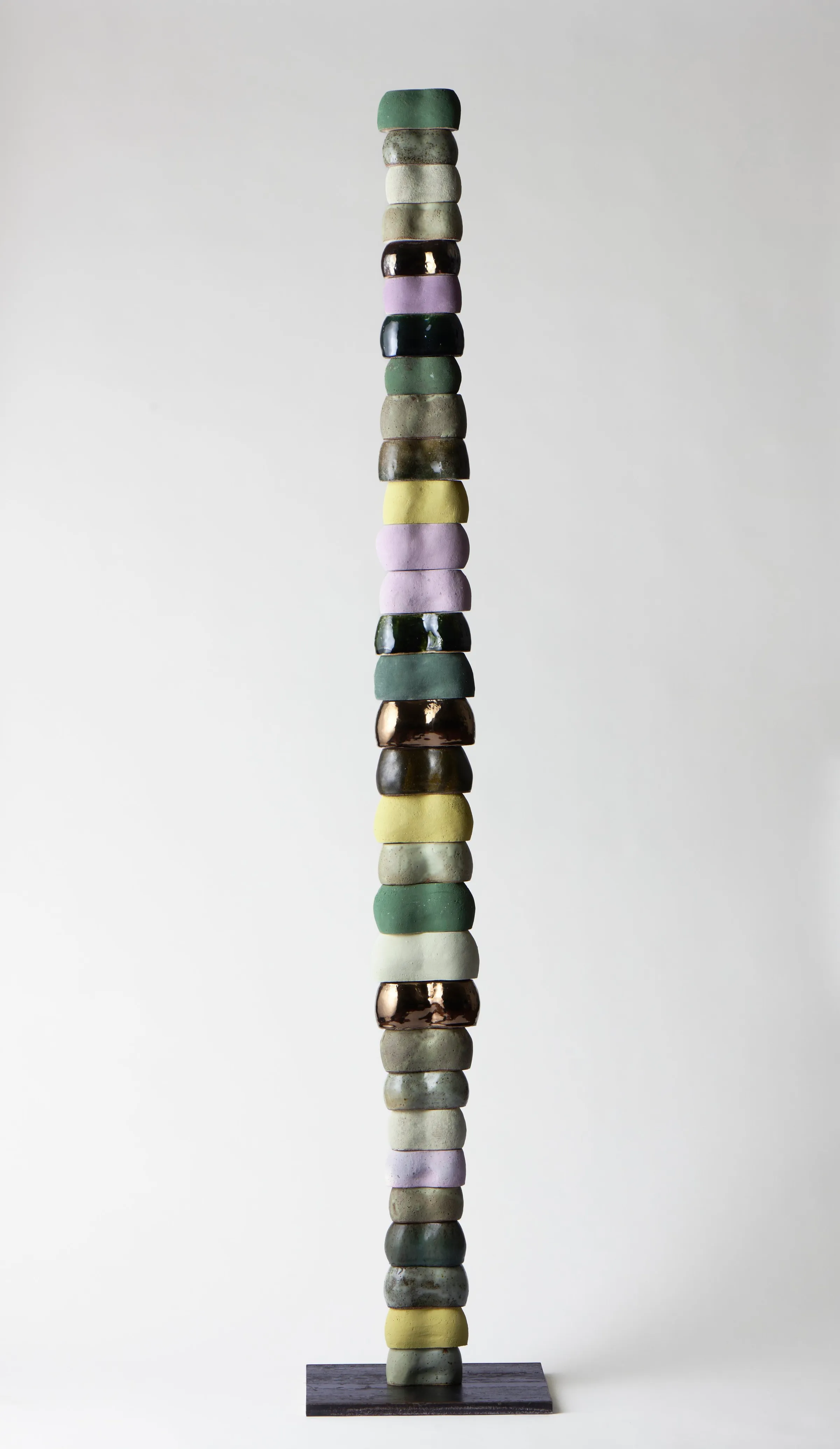 A tall column of stacked ceramic knuckle forms in greens, lilac and yellow on a steel base